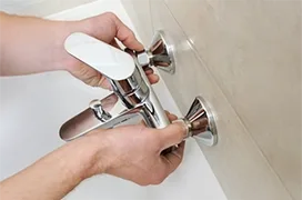 Hands install a chrome faucet handle on a wall.