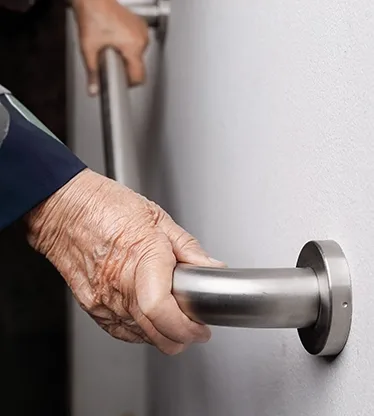 A hand holds a stainless steel grab bar on a wall.